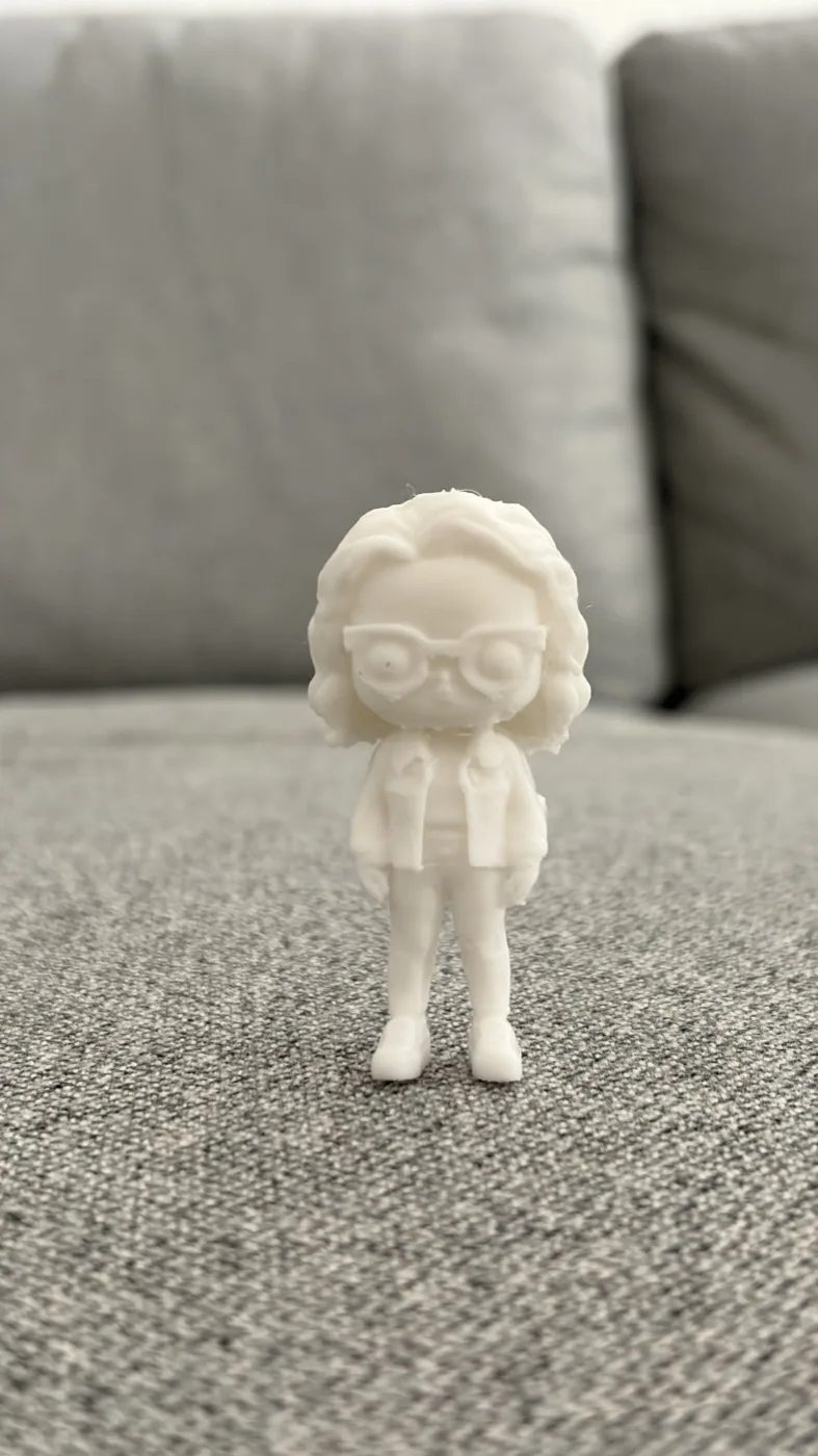 A small white 3D printed collectible figure of a woman with curly hair, glasses, and a denim jacket