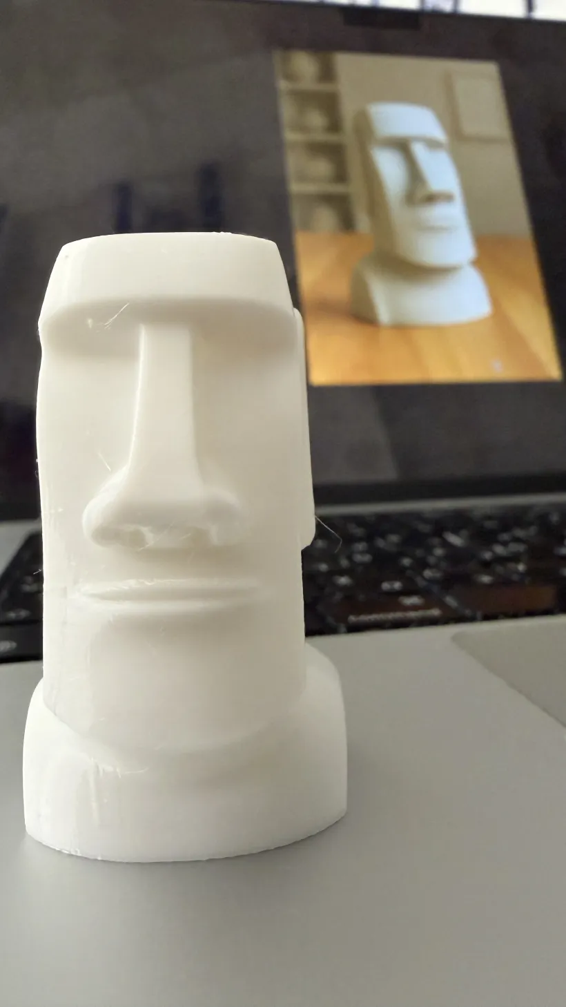 Close view of the 3D printed moai with the generated model on the laptop screen behind it